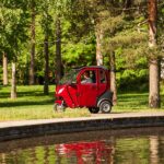 Viininpunainen Kontio Autokruiser -sähkömopoauto lammen rannalla puistossa