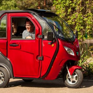 Viininpunainen Kontio Autokruiser -sähkömopoauto sivulta puistossa, kuljettaja istuu ohjaamossa