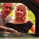 Viininpunainen Kontio Autokruiser -sähkömopoauto kuvattuna sivuikkunan läpi, ikkunassa hymyilevä pariskunta