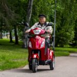 Kuljettaja ajamassa metallinpunaisella Kontio Silverfox 2.0 -senioriskootterilla puistotiellä